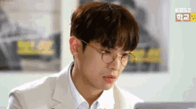 a young man wearing glasses and a suit is looking at a laptop screen .