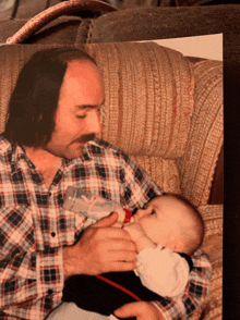 a man in a plaid shirt is holding a baby who is breastfeeding