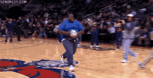 a man in a blue shirt is holding a basketball on a basketball court in front of a crowd .