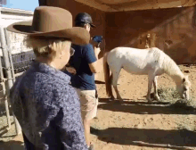 a woman in a cowboy hat is standing next to a man holding a camera in front of a horse