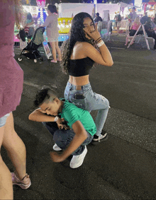 a girl in a black crop top sits on a boy 's lap at a carnival