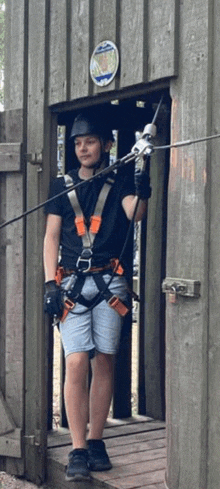 a young man wearing a helmet and a harness is standing in a wooden doorway .