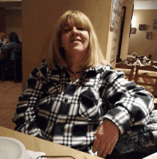 a woman is sitting at a table in a restaurant wearing a black and white plaid shirt .