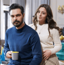 a man in a blue sweater sits next to a woman in a white sweater holding a cup of coffee