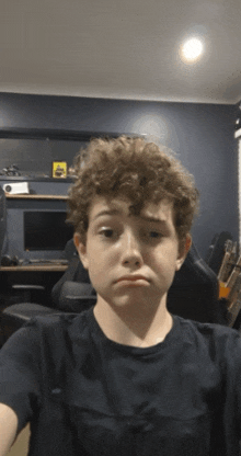 a boy with curly hair takes a selfie in front of a computer