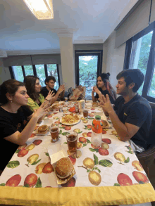 a group of people are sitting at a table with a table cloth with apples on it