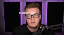 a man with glasses and a beard is standing in front of a microphone with the word croissant dev written on his face