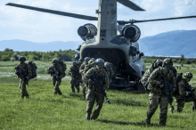 a group of soldiers are walking towards a helicopter which has the letters s-gnc on the tail