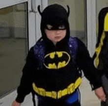 a young boy in a batman costume is walking out of a doorway .