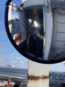 a reflection of two people taking a selfie next to an american airlines airplane