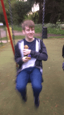 a boy is sitting on a swing eating a sandwich and smiling