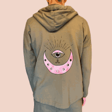 a person is wearing a green hoodie with a pink crescent moon with an eye on it