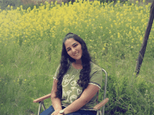 a girl wearing a green shirt that says " love me " sits in a chair in front of a field of yellow flowers