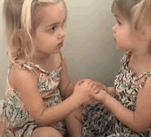 two little girls are sitting next to each other holding hands and looking at each other .