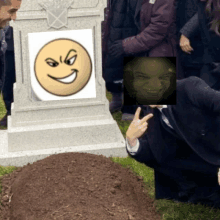 a man is kneeling in front of a grave with a picture of a smiley face on it