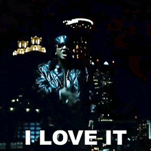 a man in a leather jacket is standing in front of a city at night and says i love it