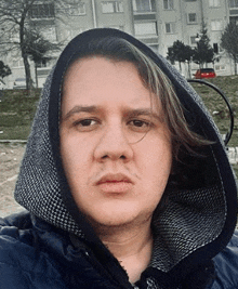 a young man wearing a hooded jacket is taking a selfie in front of a building .