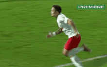 a soccer player in a white shirt and red shorts is running on a field .