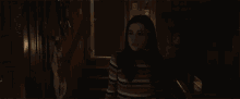 a woman in a striped shirt stands in a dark hallway