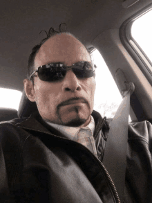 a man wearing sunglasses and a leather jacket sitting in a car