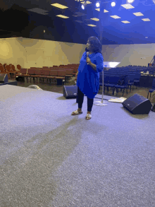 a woman in a blue shirt is standing on a stage holding a microphone