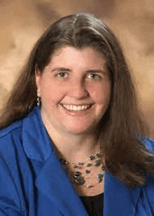 a woman is wearing a blue jacket and a necklace and smiling for the camera .