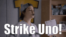a girl in a baseball uniform says strike uno in a room