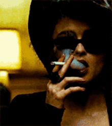 a woman wearing sunglasses is smoking a cigarette in a dark room