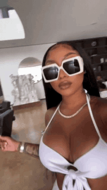 a woman wearing a white bikini top and sunglasses is taking a selfie .