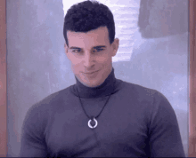 a man wearing a turtleneck and a horseshoe necklace smiles for the camera