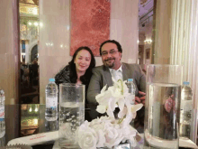 a man and a woman are sitting at a table with bottles of water and vases of flowers