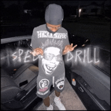 a man wearing a t-shirt that says hell side drill is standing next to a car