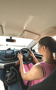 a woman in a pink top is driving a car with a tata logo on the steering wheel