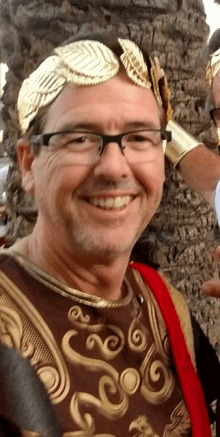 a man wearing glasses and a gold laurel wreath smiles