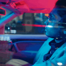 a man wearing glasses and a necklace is driving a car at night