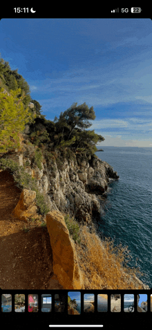 a phone screen shows a cliff overlooking a body of water at 15:11