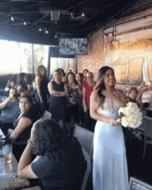 a woman in a wedding dress is holding a bouquet of flowers in front of a group of people .