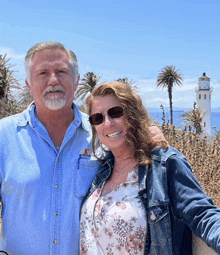 a man and a woman pose for a picture with a lighthouse in the background