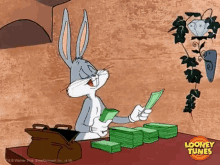 bugs bunny from looney tunes is sitting at a table holding a stack of money .