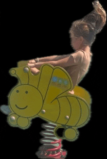 a little girl is sitting on a yellow bee shaped spring ride