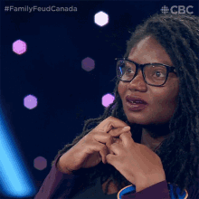 a woman wearing glasses and a purple shirt is sitting in front of a screen that says family feud canada