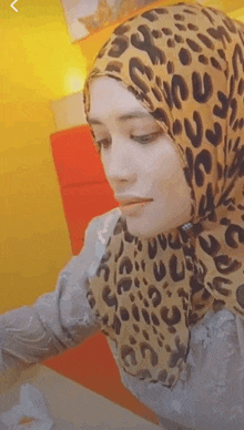 a woman wearing a leopard print scarf is sitting at a table with a yellow background .