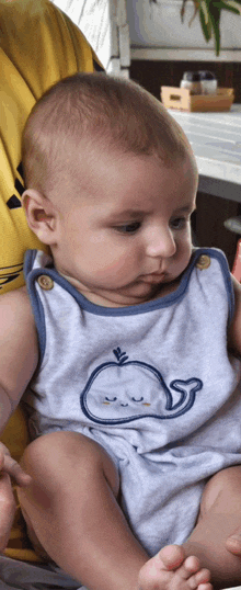 a baby with a whale on his shirt is sitting in a chair