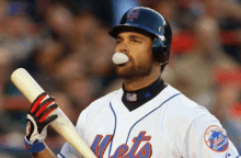 a mets baseball player holds a bat in his mouth