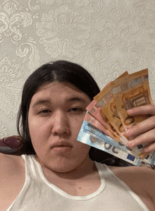 a woman in a white tank top holds a bunch of euro bills in her hand