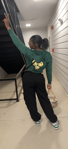 a woman wearing a green hoodie with smiley faces on the back is standing in a hallway