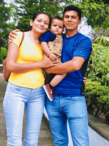 a man in a blue shirt holds a baby while a woman in a yellow shirt looks on