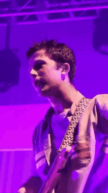 a man playing a guitar in front of a purple backdrop