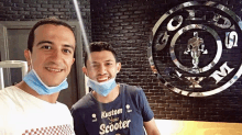 two men wearing face masks pose for a picture in front of a gym logo