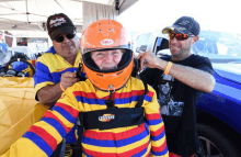 a man wearing an orange bell helmet is being helped by two other men